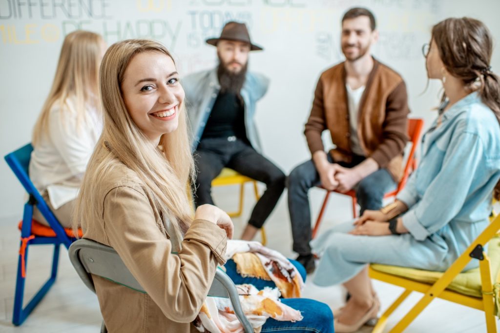 Portrait of a smiling woman sitting in a circle with group of people during the psychological training in the white office