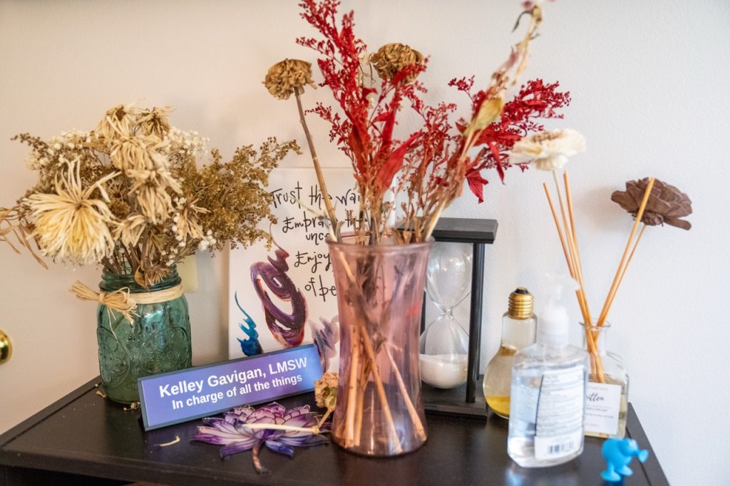 A close-up view of a purple glass vase filled with dried botanicals on a shelf next to welcoming decor inside a River's Bend, P.C. clinic space.