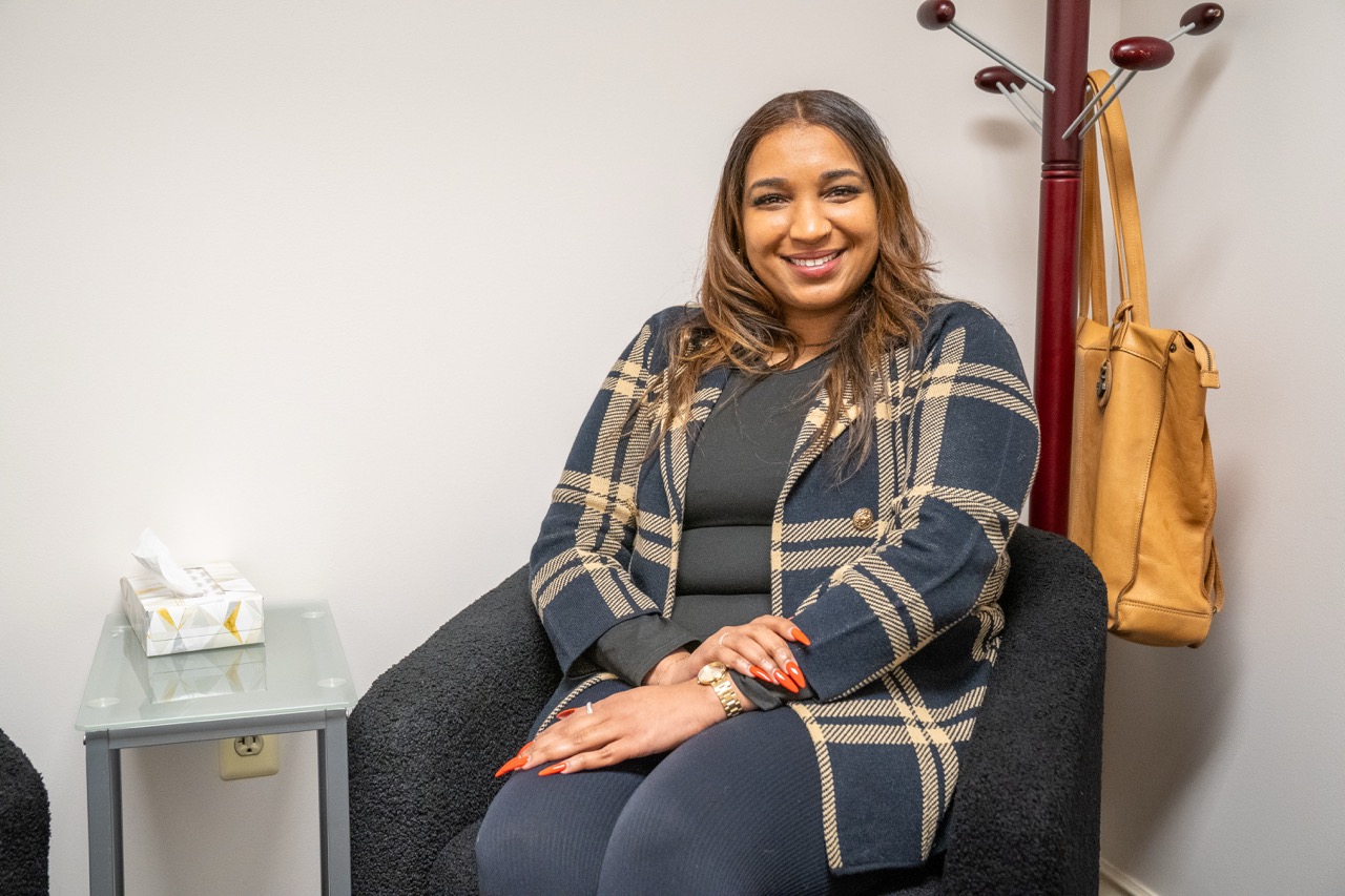 Psychiatric Nurse Practitioner Chanel Graham, MSN, PMHNP, smiling and wearing a plaid blazer while sitting in a therapy room at River's Bend, P.C.