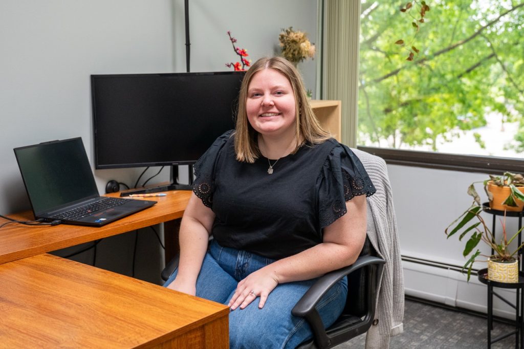 A welcoming clinical staff member smiling at her office desk at River's Bend, P.C. in Madison Heights, Michigan.