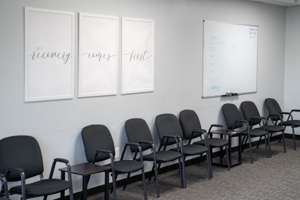 A structured PHP group therapy room at River's Bend, P.C. featuring rows of black chairs, a whiteboard on the wall, and bright lighting.