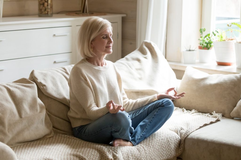 A woman practicing meditation on a couch, building healthy habits for mental health at home.