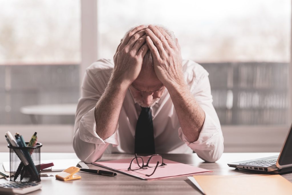 A stressed businessman sitting at a desk with his head in his hands, reflecting employee burnout in workplace settings.