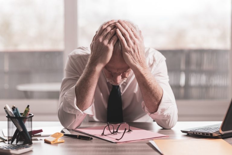 A stressed businessman sitting at a desk with his head in his hands, reflecting employee burnout in workplace settings.