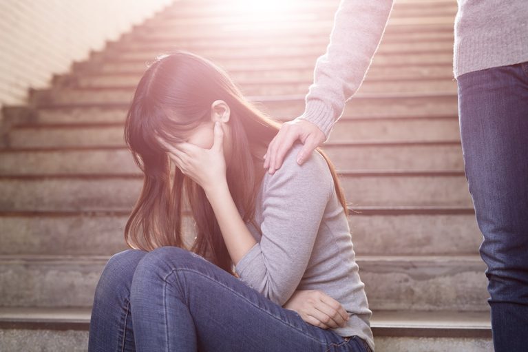 A supportive friend comforting a depressed woman sitting on underground steps.