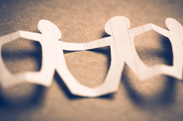 Paper cutouts of human figures joining hands to form a continuous chain.