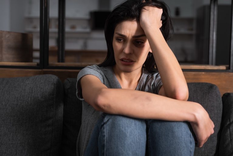 A person sitting on a sofa with their arms wrapped around their knees, reflecting emotional distress and trauma.