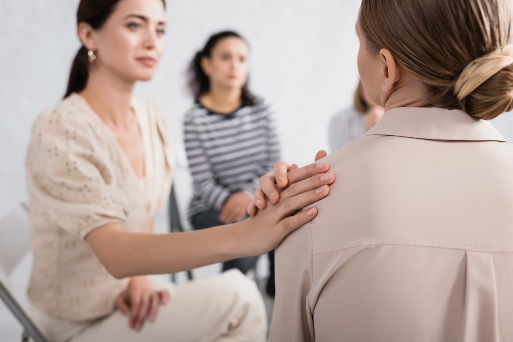 A supportive woman listening attentively and offering comfort to a stressed colleague in an office setting.